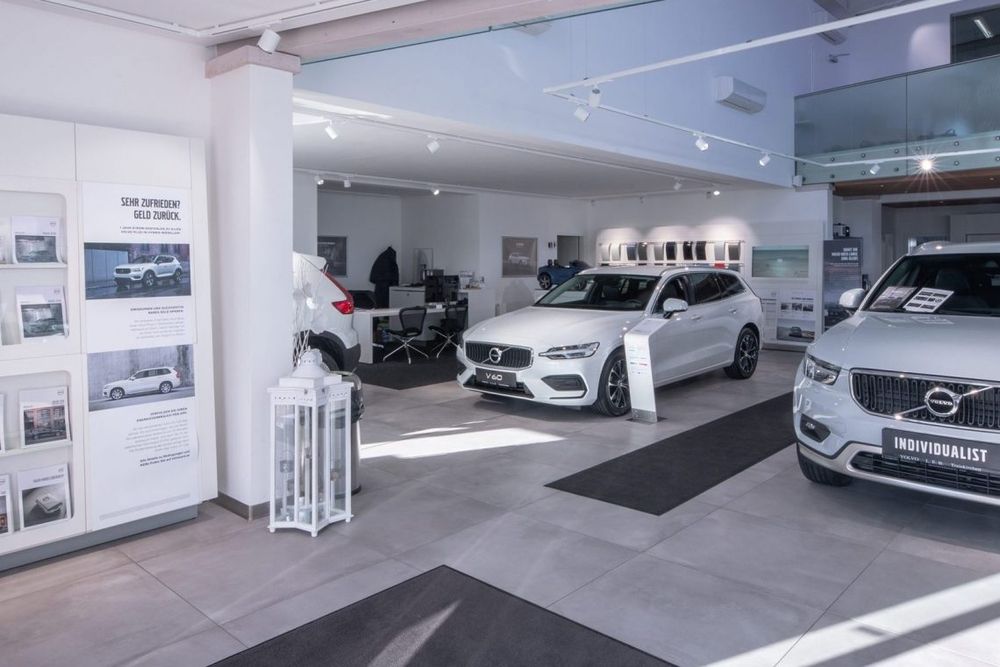 Moderner Innenraum eines Autohauses mit zwei ausgestellten Fahrzeugen und Werbematerialien.